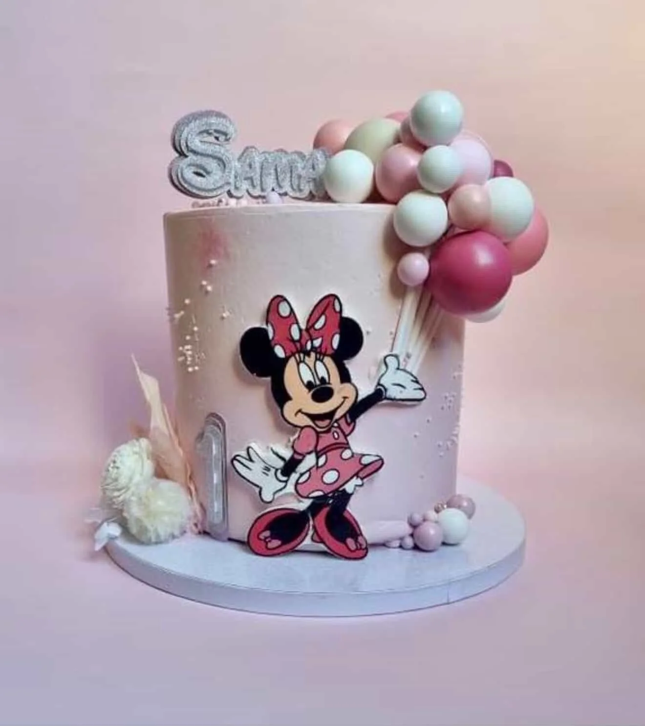 A pink birthday cake decorated with Minnie Mouse and a variety of pastel-colored balloons, with the word 'Sprinkle' on top.