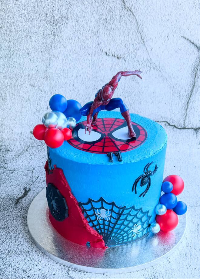 Spider-Man themed birthday cake with Spider-Man figure on top, decorated with red, blue, and silver balls, featuring web and spider designs on the sides.