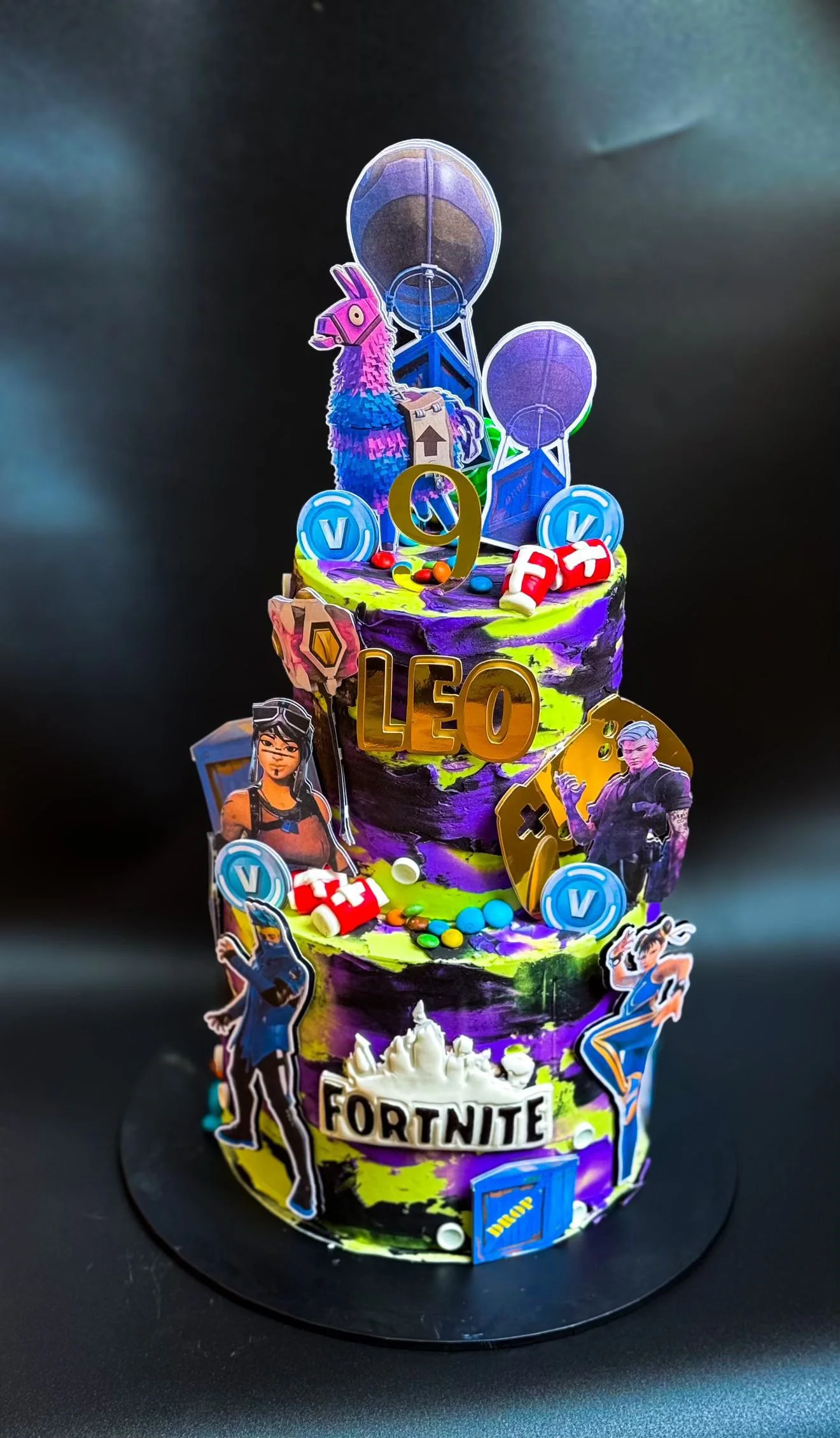 Colorful Fortnite-themed birthday cake decorated with characters, symbols, and items from the game, with a large number 9 on top.
