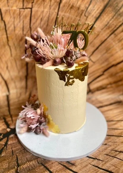 A gold and pink birthday cake with floral decorations and a "Happy 16" topper, placed on a white cake board against a wooden background.
