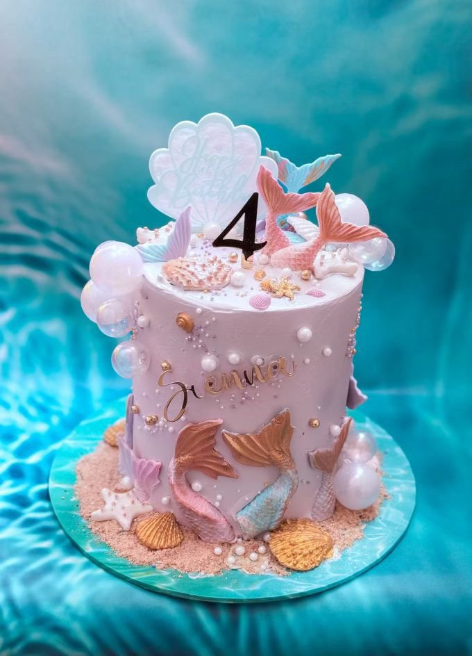 Sea-themed birthday cake with mermaid decorations, pearls, starfish, seashells, and pink starfish toppers, featuring the name 'Juenny' and a large number 4.