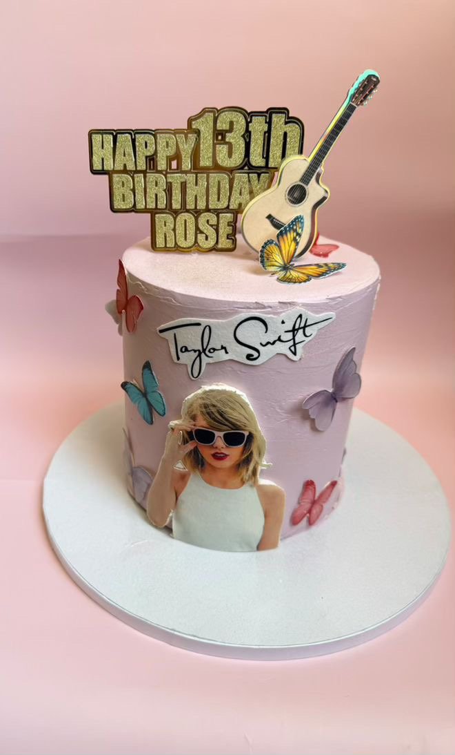 Pink birthday cake with Taylor Swift's name, colorful butterflies, a guitar topper, and a photo of a girl with sunglasses on it.