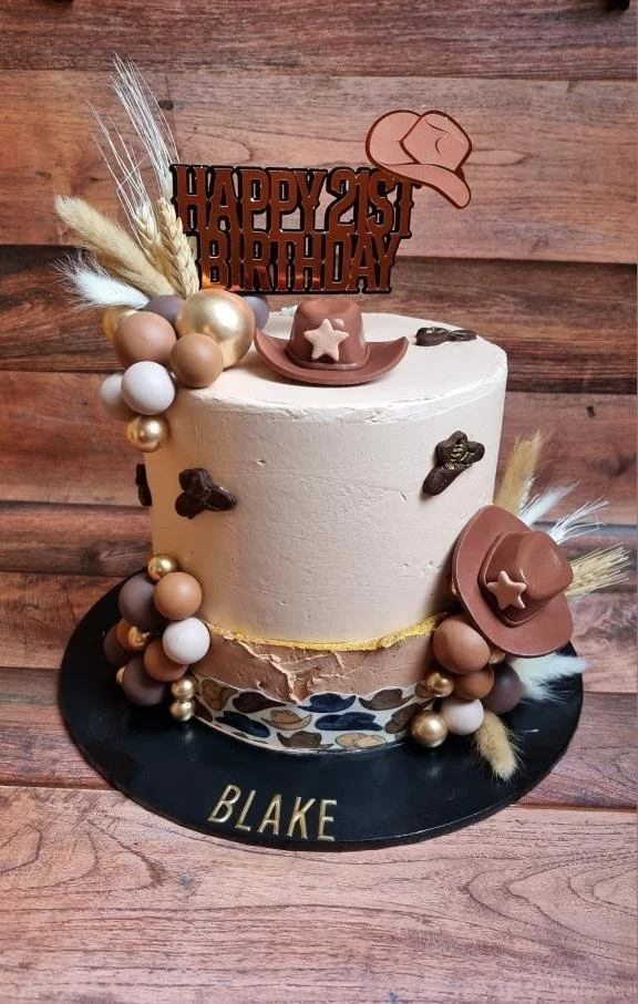 A cowboy-themed birthday cake decorated with chocolate hats, stars, and feathers, with a "Happy 21st Birthday" topper and the name "Blake" on the base.