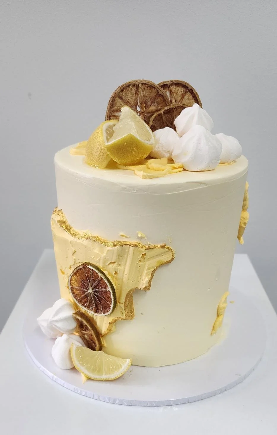 White cake decorated with lemon slices, dried citrus, whipped cream, and lemon curd on top and on the side.