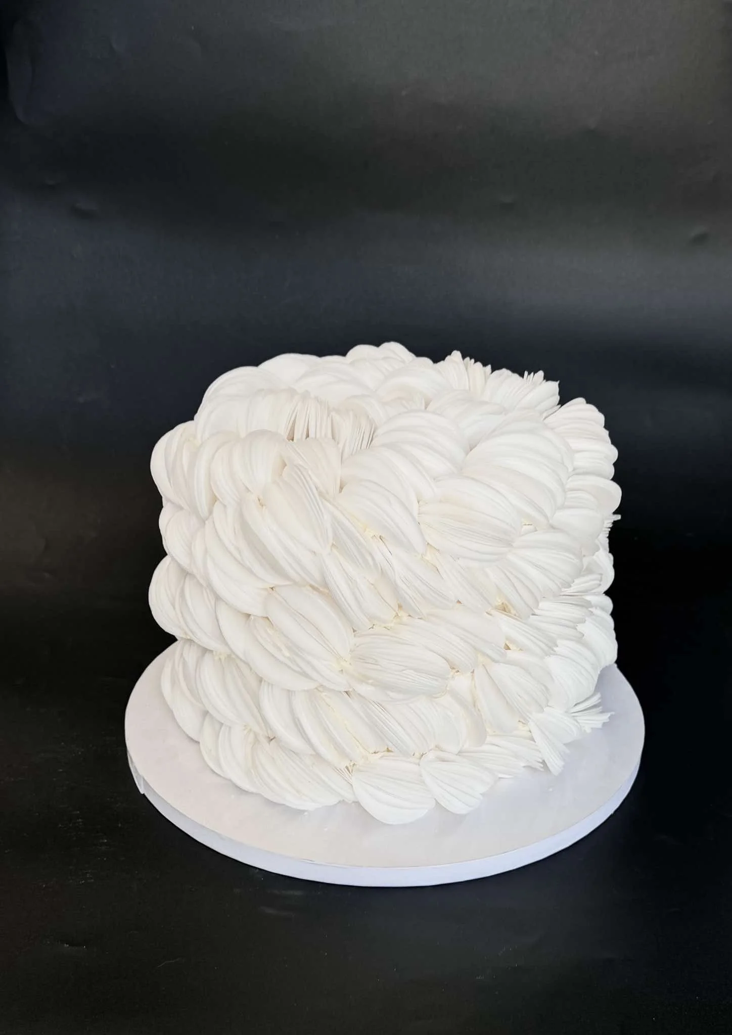A white layered cake decorated with rosette frosting on top, placed on a round white cake board against a black background.