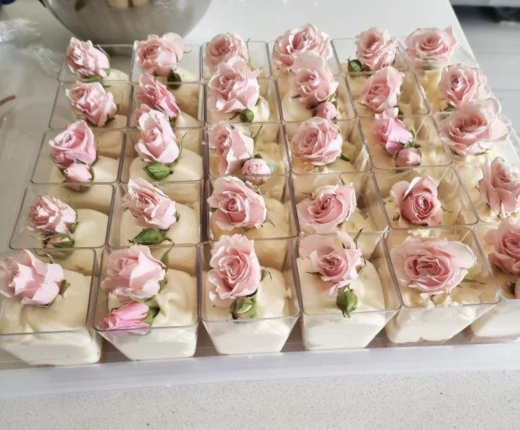 A tray of individual dessert cups topped with pink roses and green buds, arranged in neat rows.