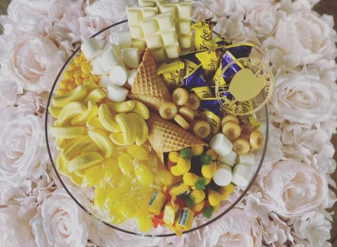 Yellow and white candies arranged in a decorative glass bowl on a floral tablecloth.