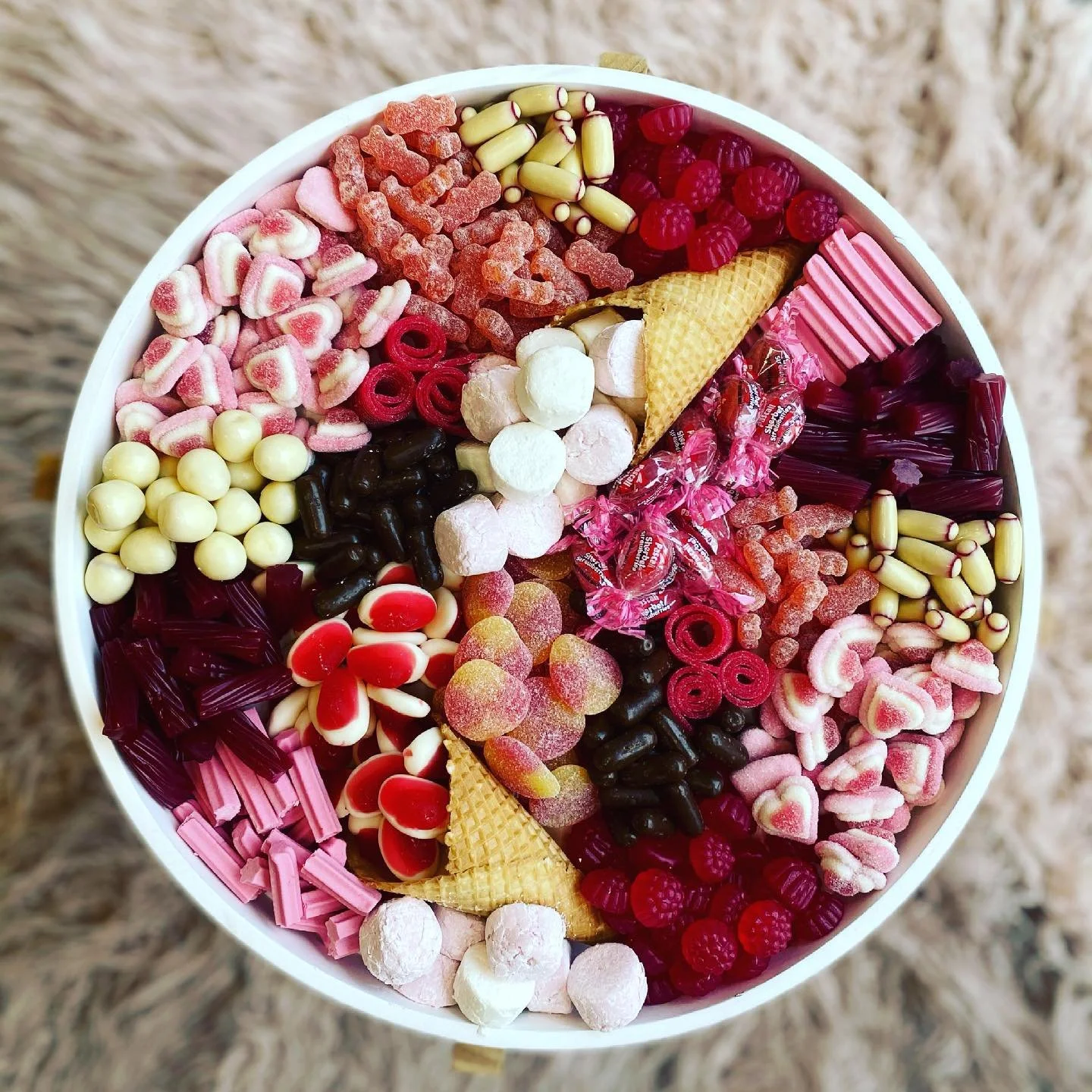 A round container filled with various colorful candies, including gummies, lollipops, and chocolates arranged in sections.