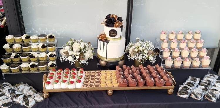 Dessert table with cupcakes, a tiered cake topped with flowers, and floral arrangements for a celebration.