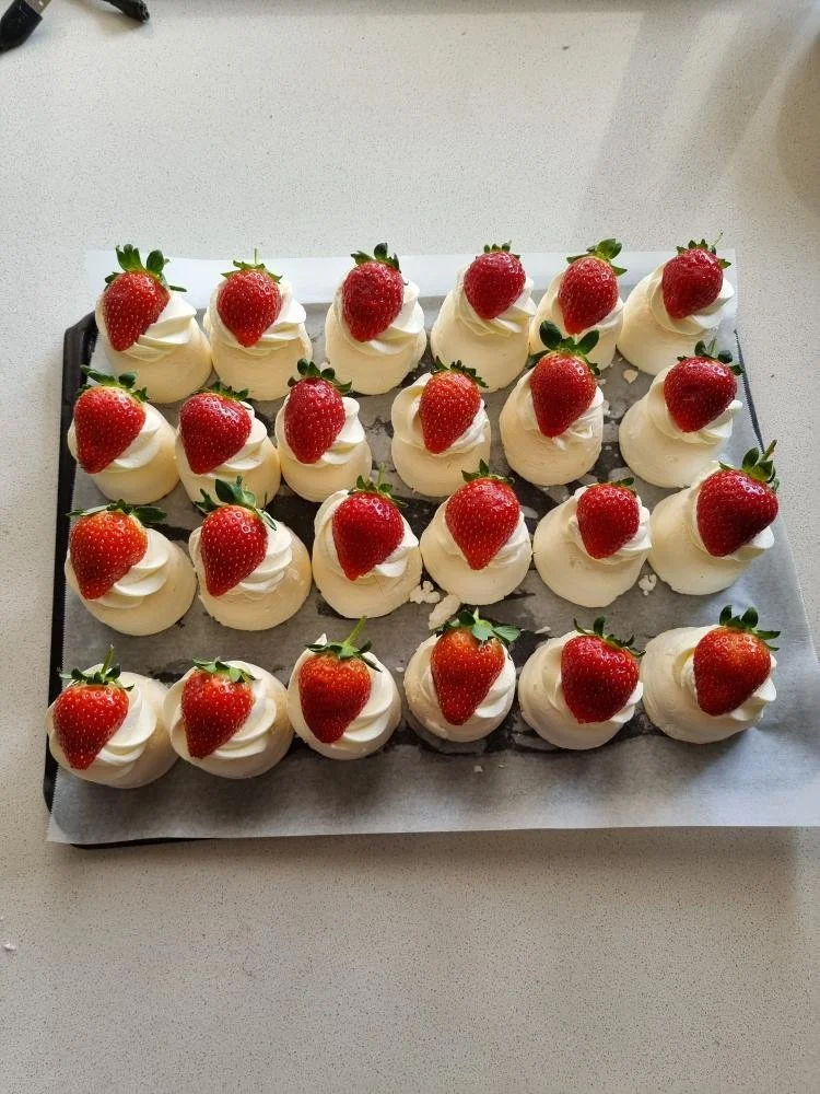 Tray of strawberries topped with whipped cream and green leaves.