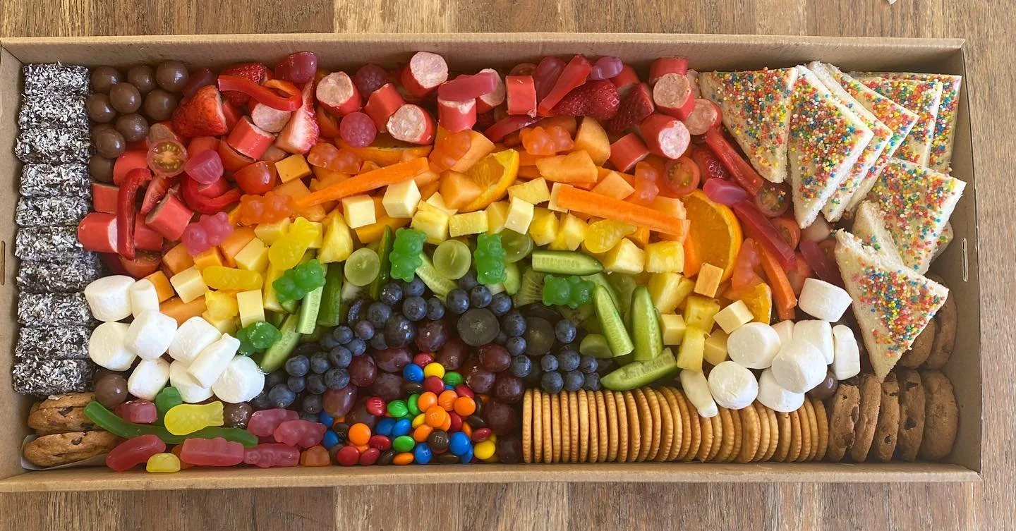 A colorful assortment of candies and treats arranged in a tray, including chocolate-coated candies, gummy worms, berries, fruit-shaped candies, marshmallows, cookies, and decorated sugar cookies.