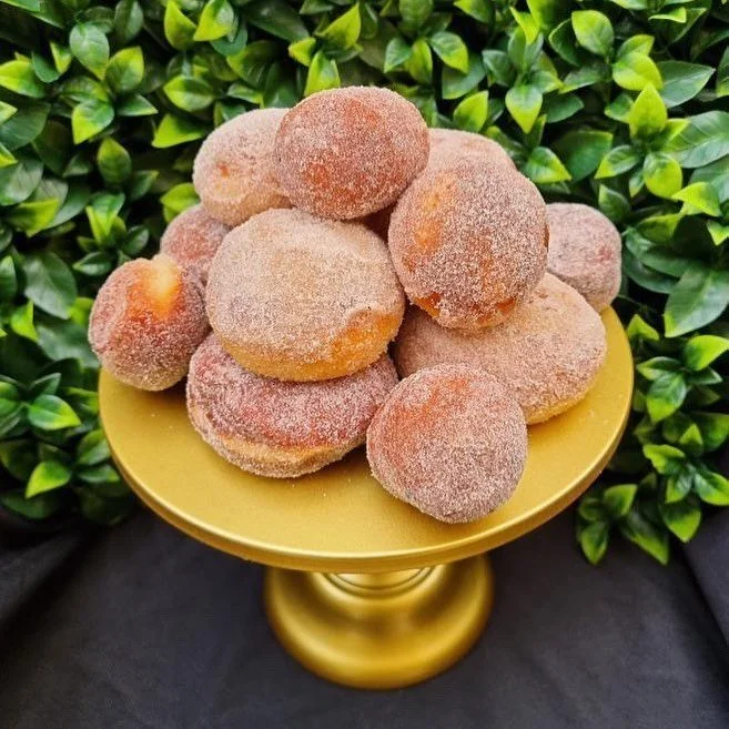 Frosted sugar-coated donuts arranged on a yellow cake stand with green leafy background.