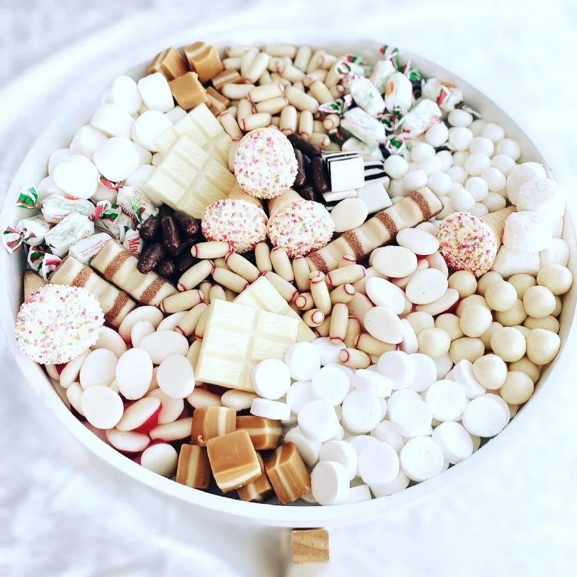 A round white tray filled with assorted candies, including chocolate bars, peppermint candies, white and brown candies, and colorful sprinkled treats.