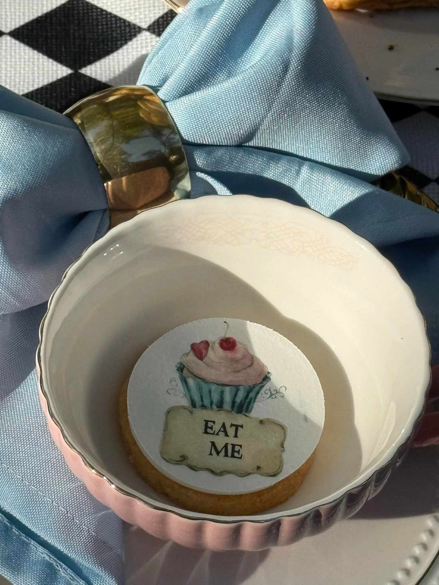A decorative cake with a cupcake design on an edible topper and the words "EAT ME" written on it.