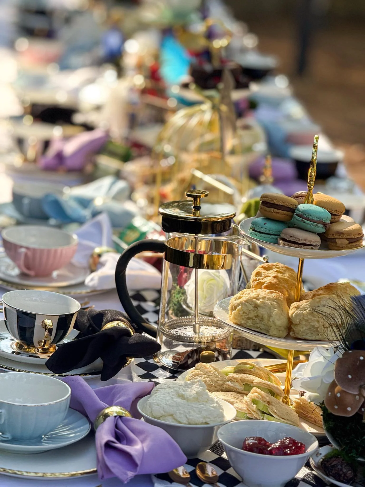 A table set for a meal with various desserts, croissants, and tea cups, decorated with purple napkins and gold accents.