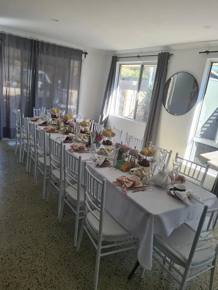 A dining table set for a meal in a bright room with white walls and a window with curtains.