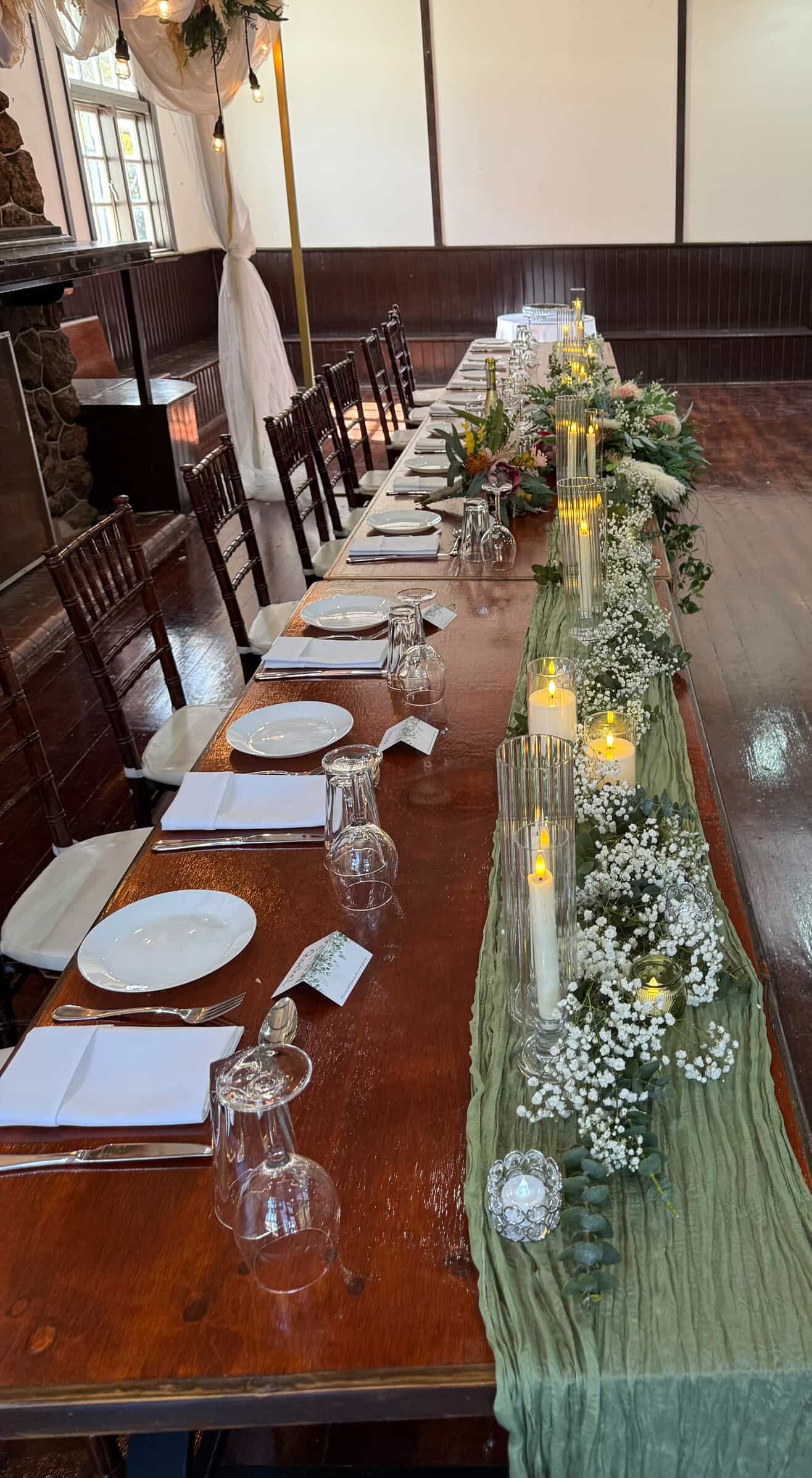 Decorated dining table with white plates, glasses, silverware, candles, and floral arrangements for a special event or celebration.