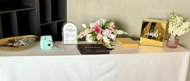 Decorative table with a floral arrangement, a small blue Instant Camera, and various cards and signs.