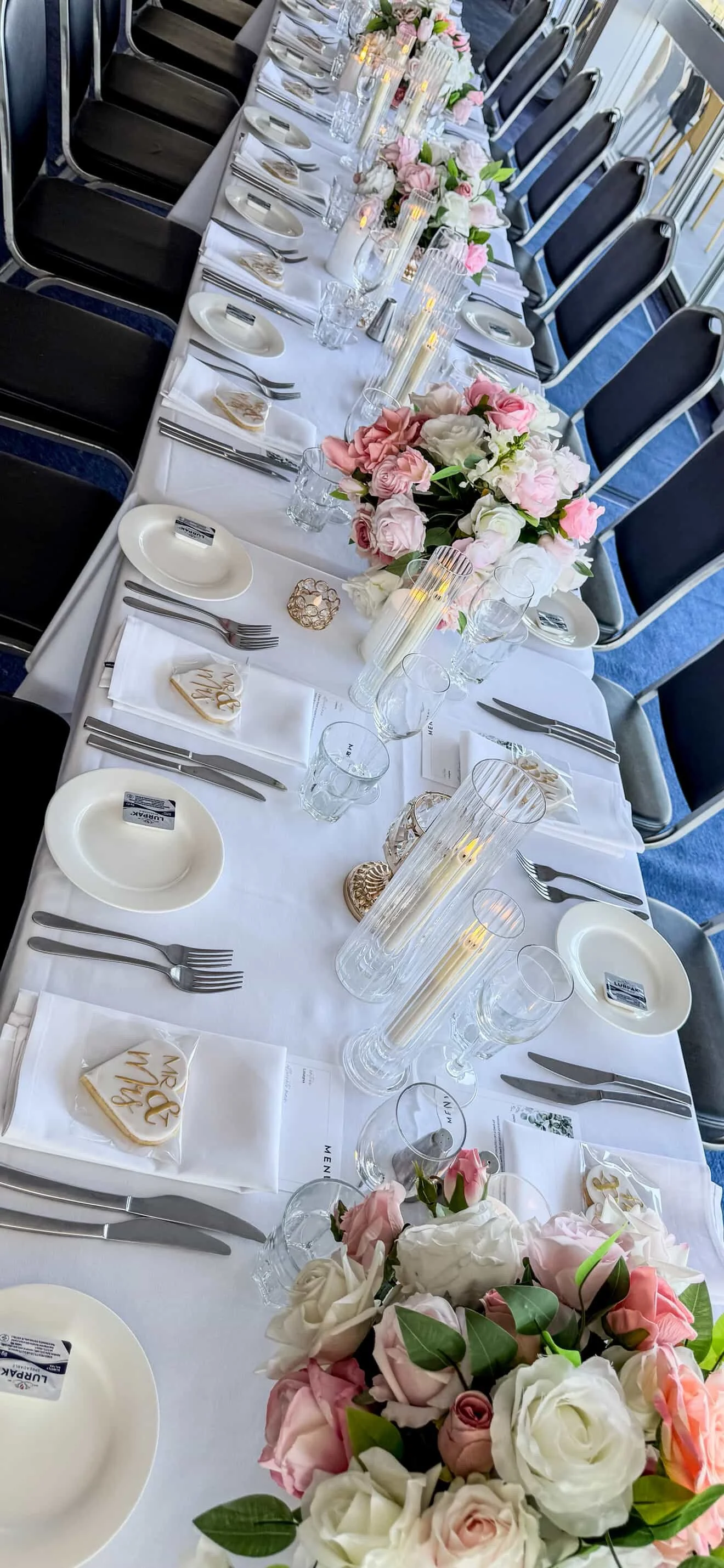 Elegant banquet table set with floral centerpieces, candles, glassware, and place settings with white plates and silverware.