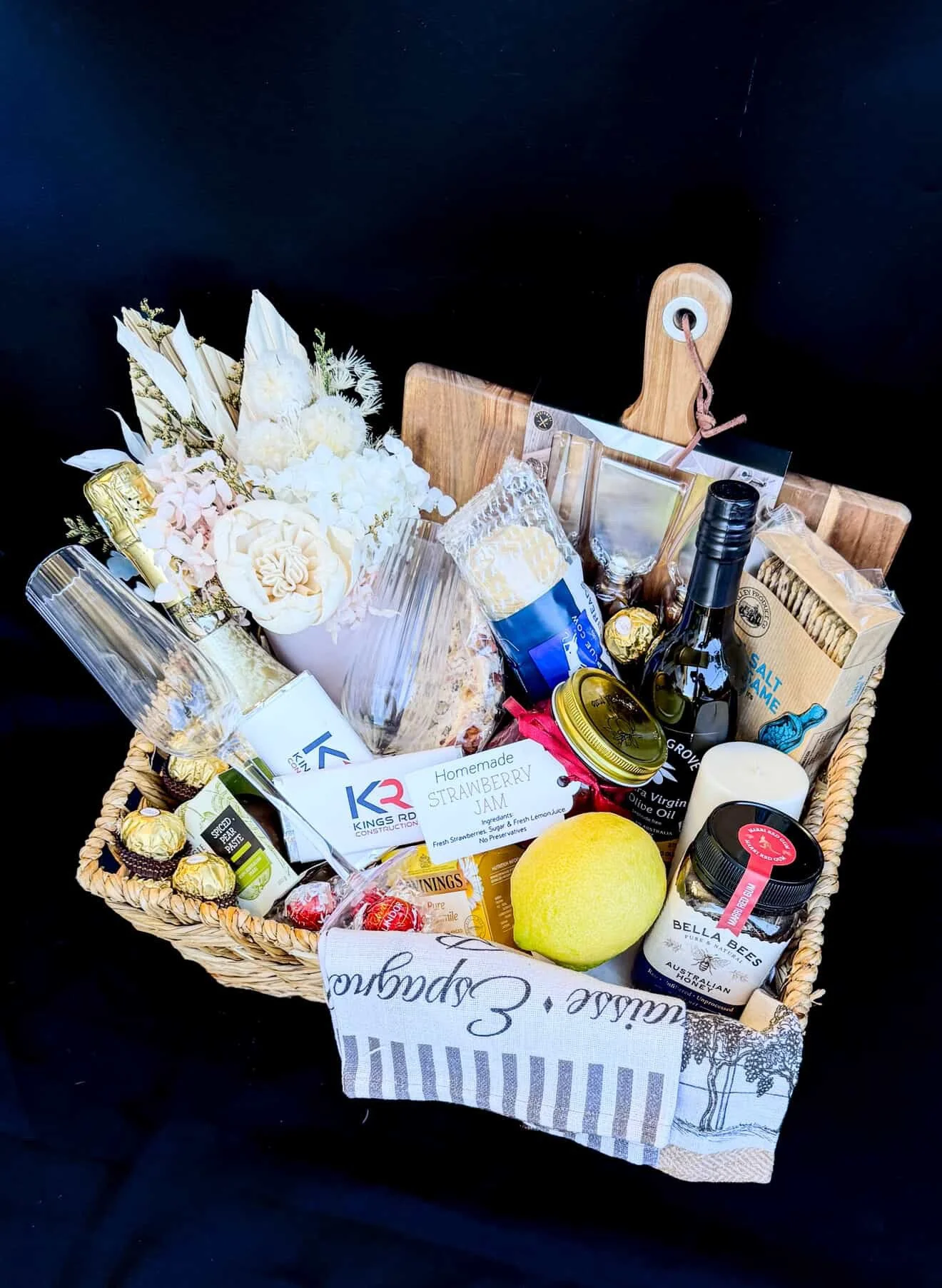 A gift basket filled with various items including flowers, snacks, beverages, and a lemon, set against a black background.