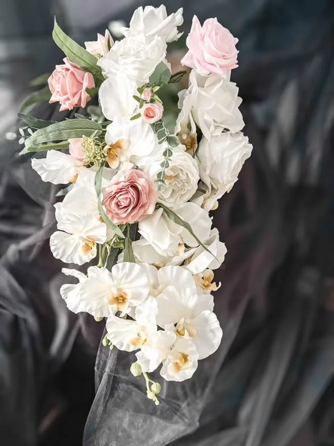 A bouquet of white and pink roses and white orchids wrapped in clear plastic.