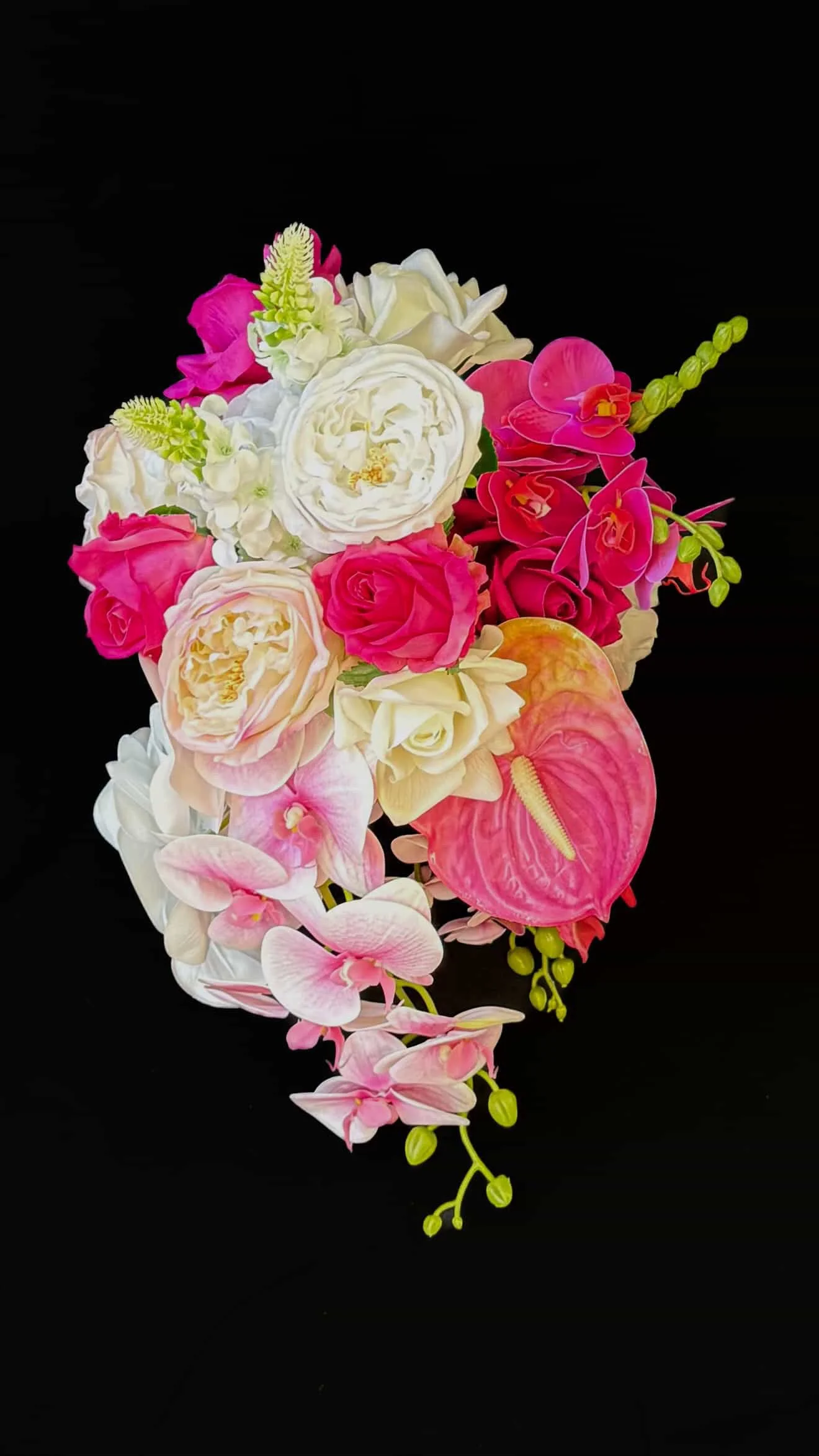 Arrangement of pink, white, and cream flowers including orchids, roses, and anthuriums on a black background.