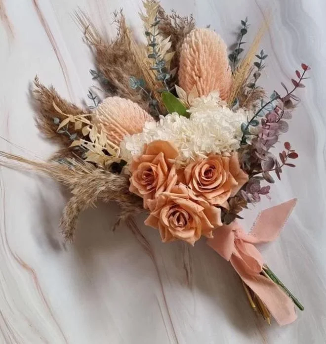 A bouquet of dried and preserved flowers including roses, pampas grass, and hydrangeas, tied with a pink ribbon.