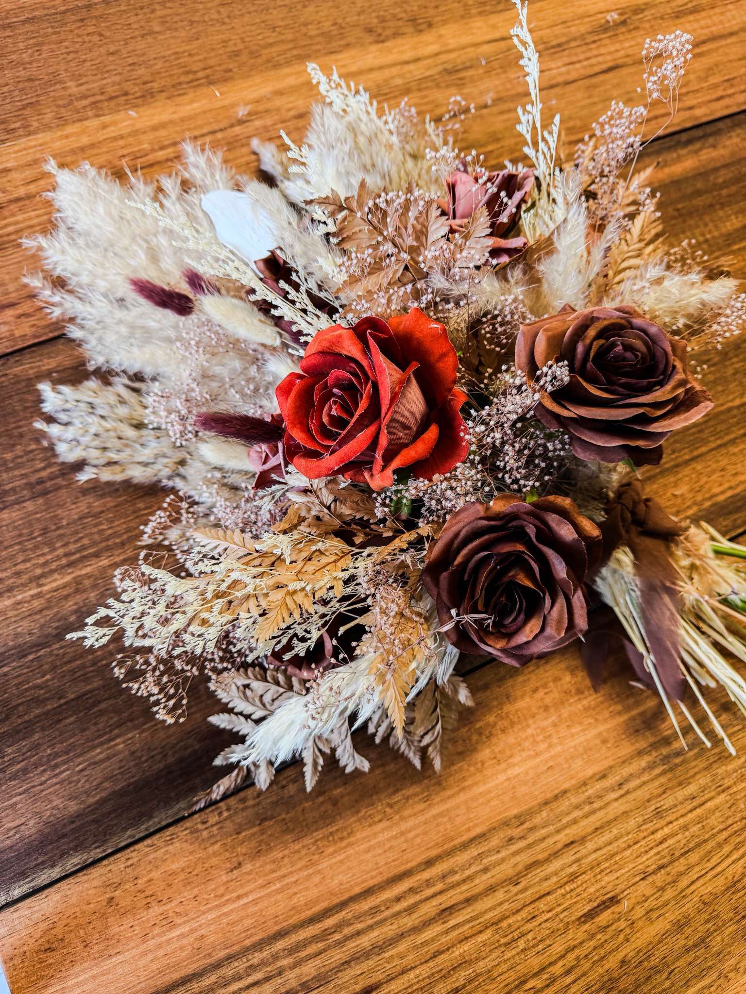 A bouquet of dried flowers featuring various roses, grasses, and foliage on a wooden surface.