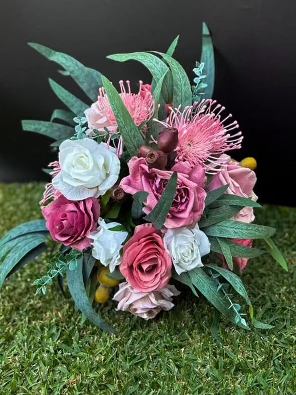 A bouquet of pink, white, and purple artificial flowers with greenery, displayed on grass against a black background.