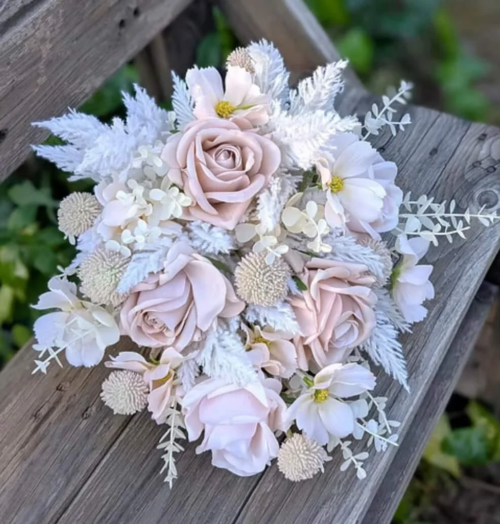 A bouquet of pale pink roses, white flowers, and greenery resting on a wooden surface.