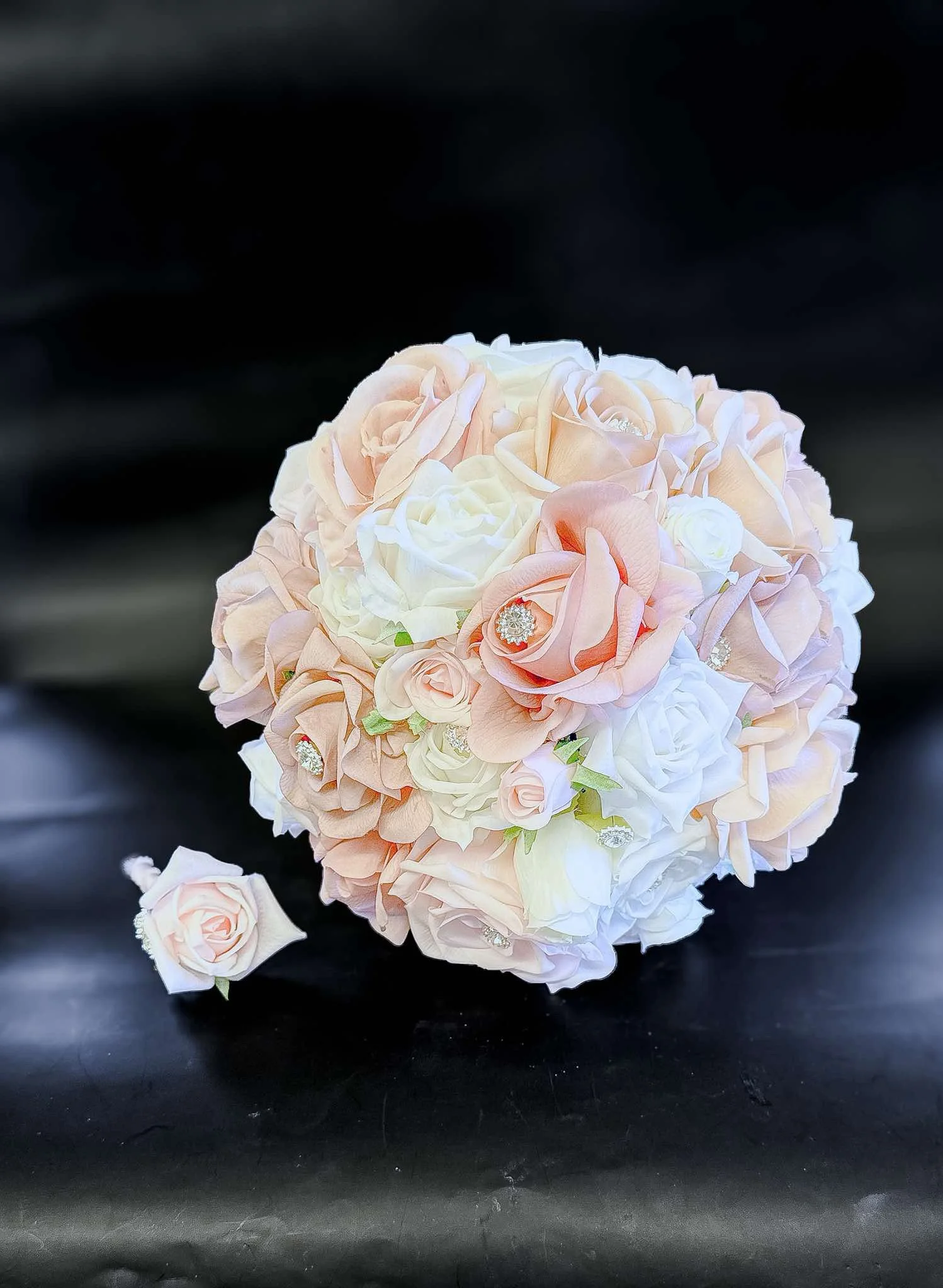 A bouquet of light pink and white roses with some green foliage on a reflective black surface.