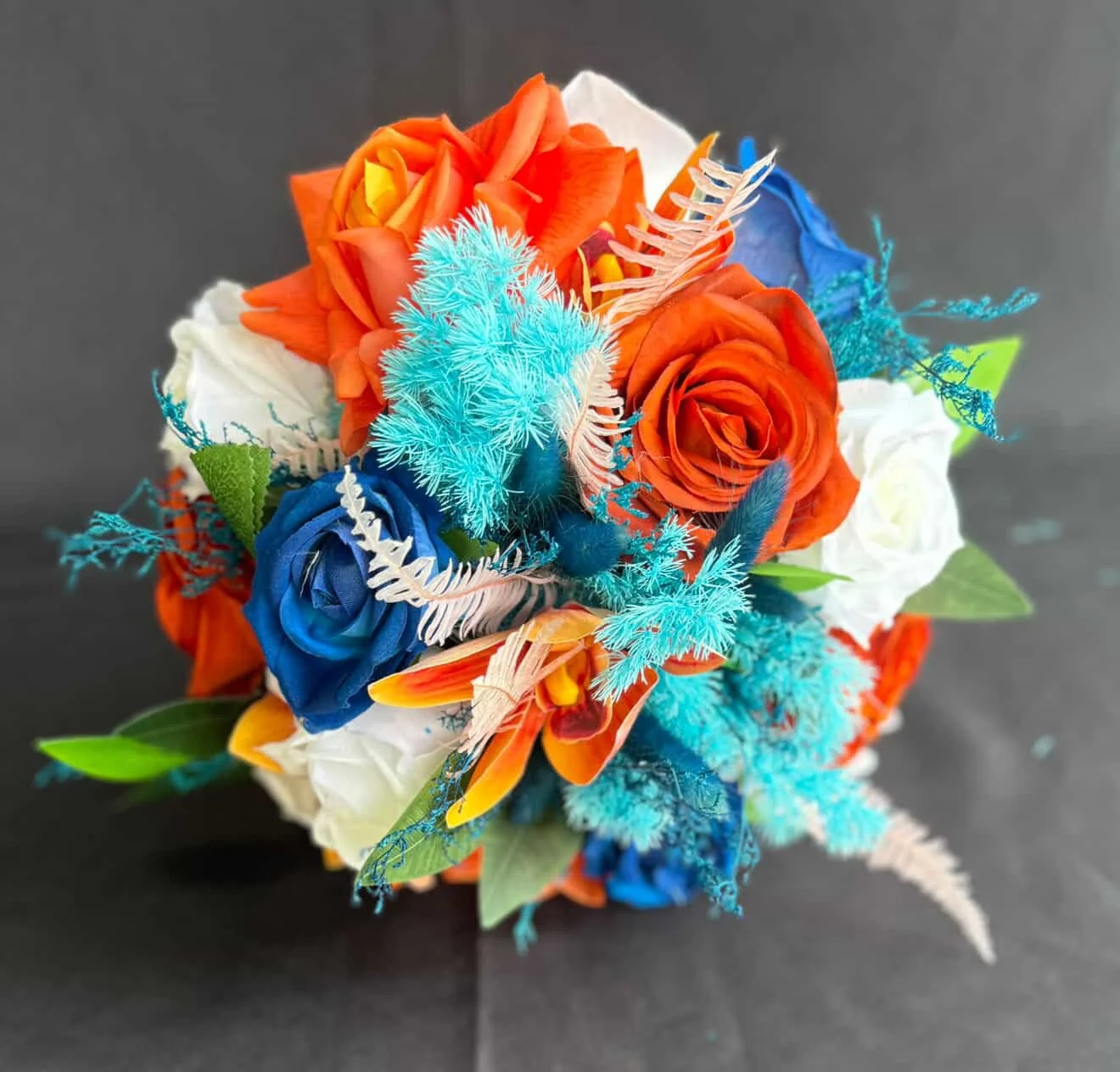 A colorful artificial flower bouquet with orange, blue, white roses, and blue and white decorative foliage against a black background.