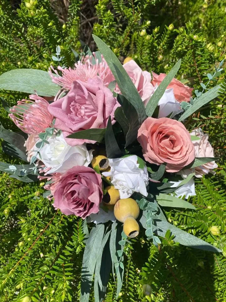 A bouquet of pink, white, and light purple flowers with green leaves, placed on a background of green foliage.