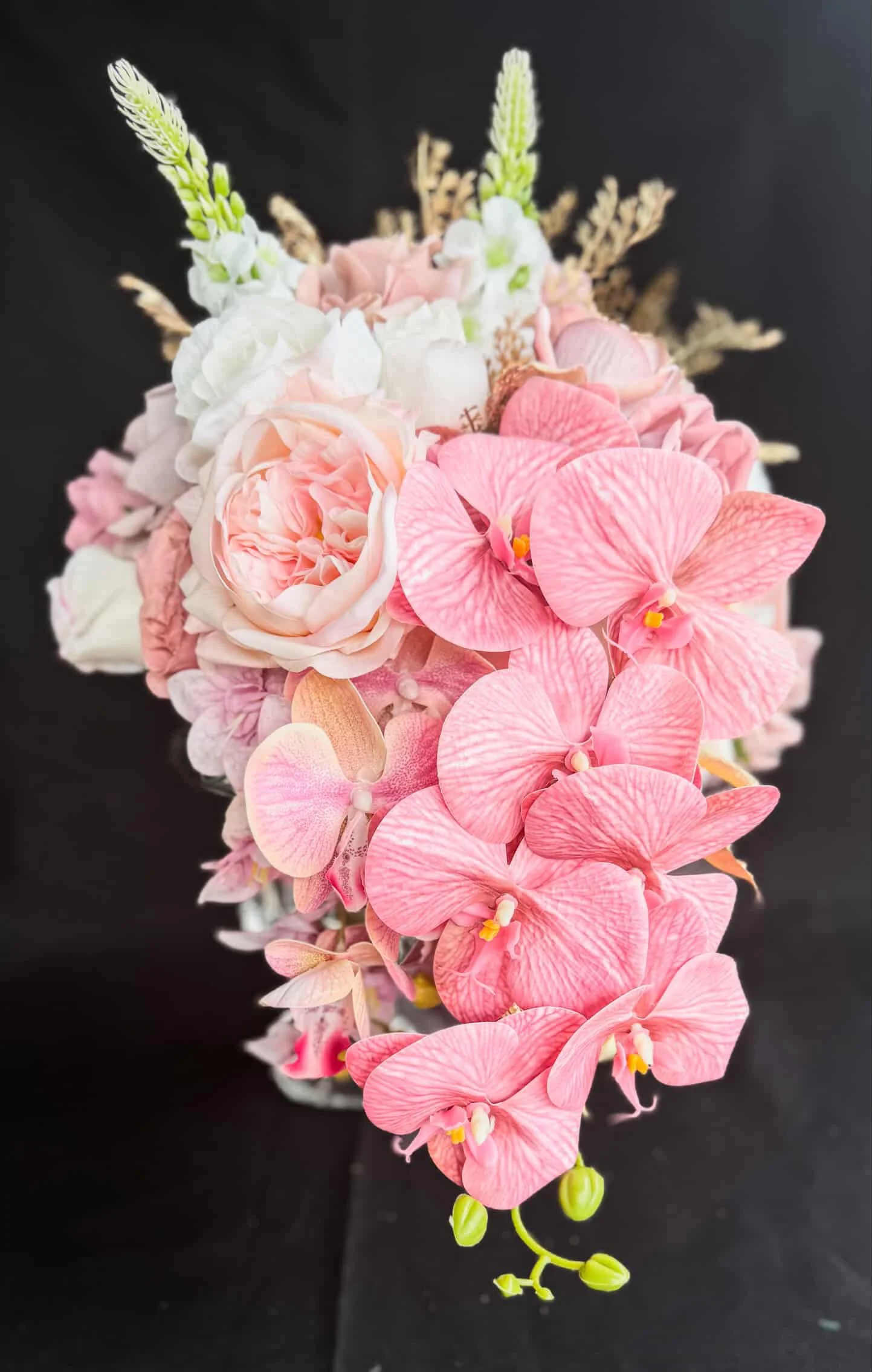 A bouquet of pink, white, and cream flowers, including orchids and roses, against a black background.