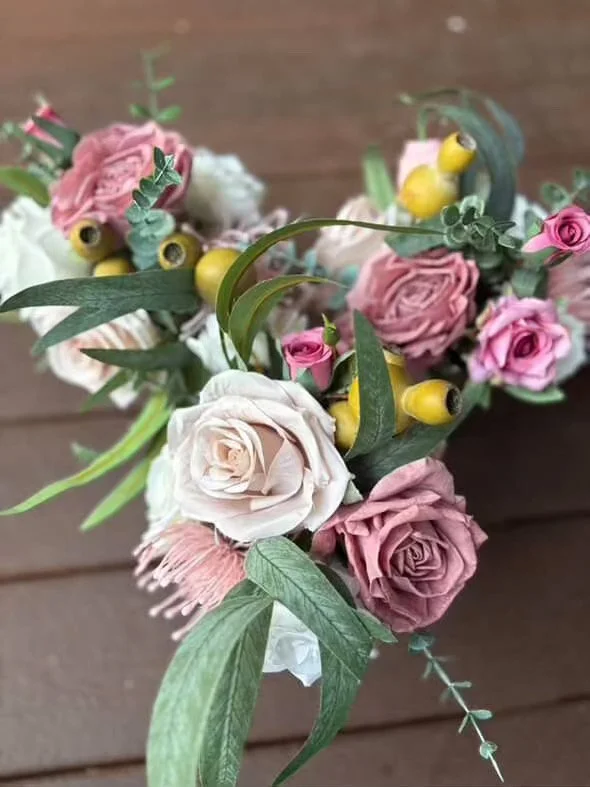 A floral arrangement with pink and white roses, yellow berries, and greenery on a wooden surface.