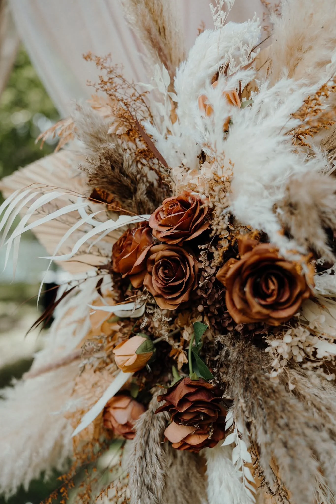 Close-up of a dried flower bouquet with brown roses, beige and white pampas grass, and dried foliage.