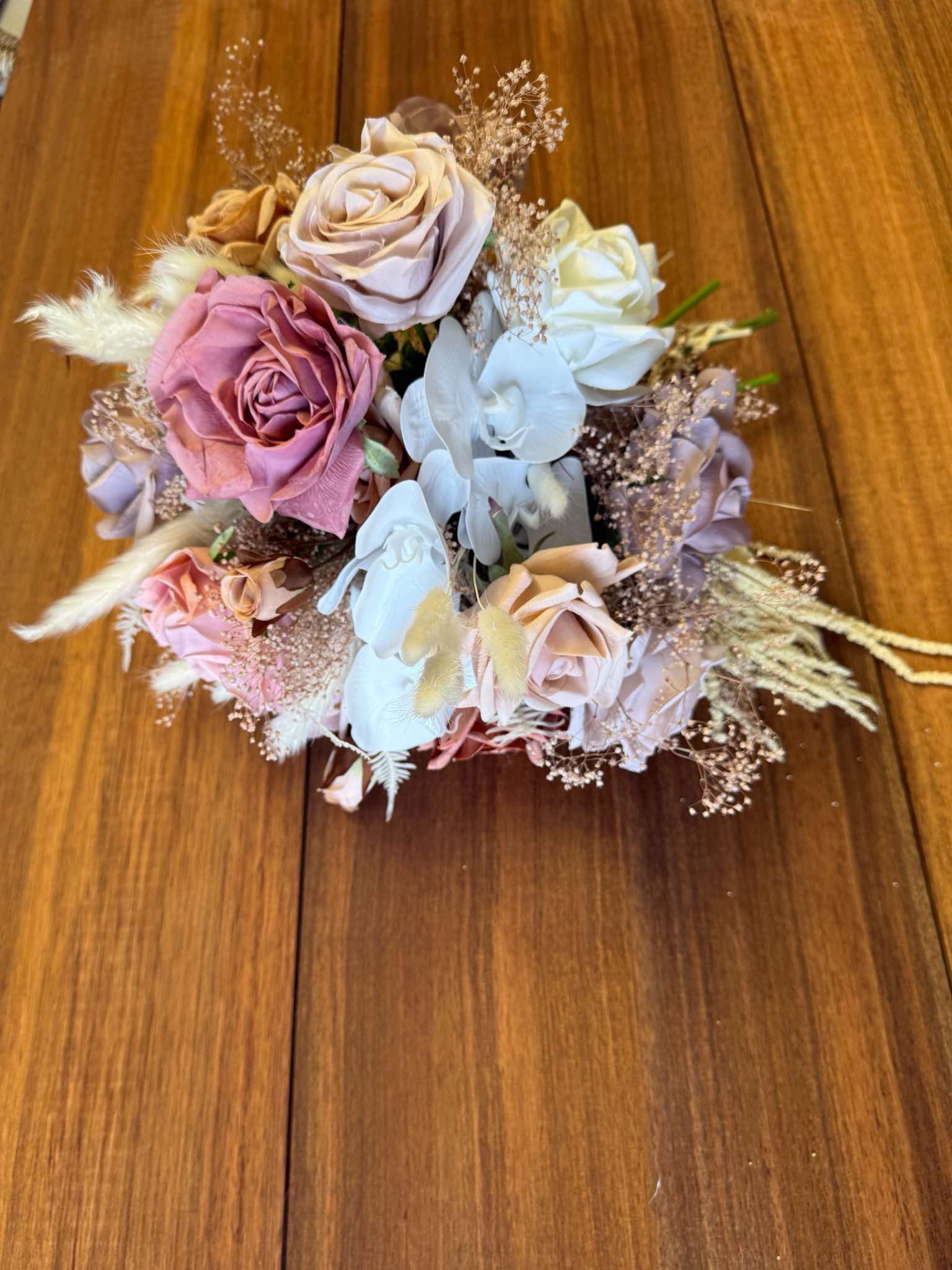 A bouquet of mixed roses and dried flowers on a wooden surface.
