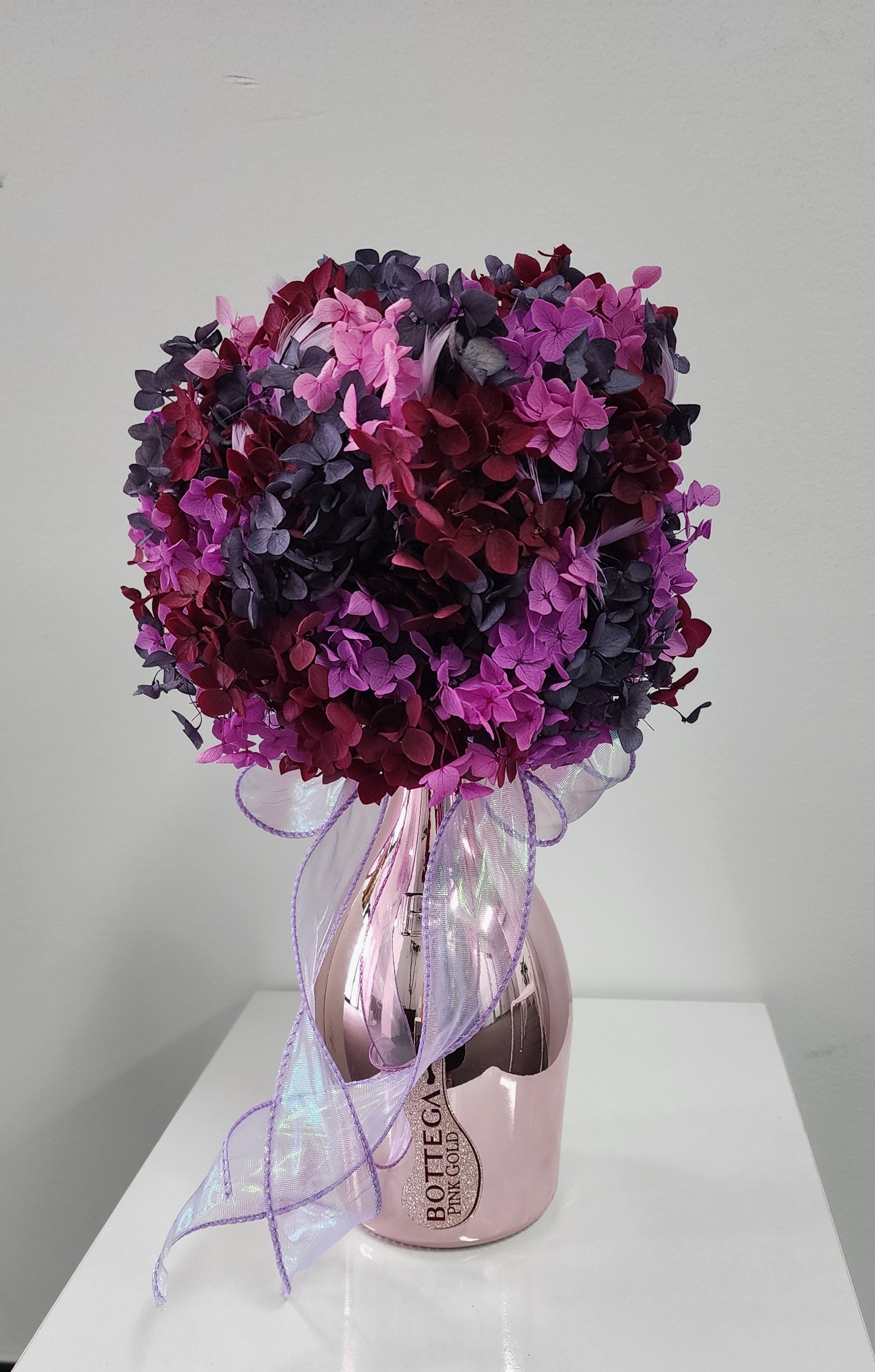 A bouquet of pink and purple artificial flowers in a pink vase with a ribbon, labeled "BOTTLE HEAD PINK GOLD".