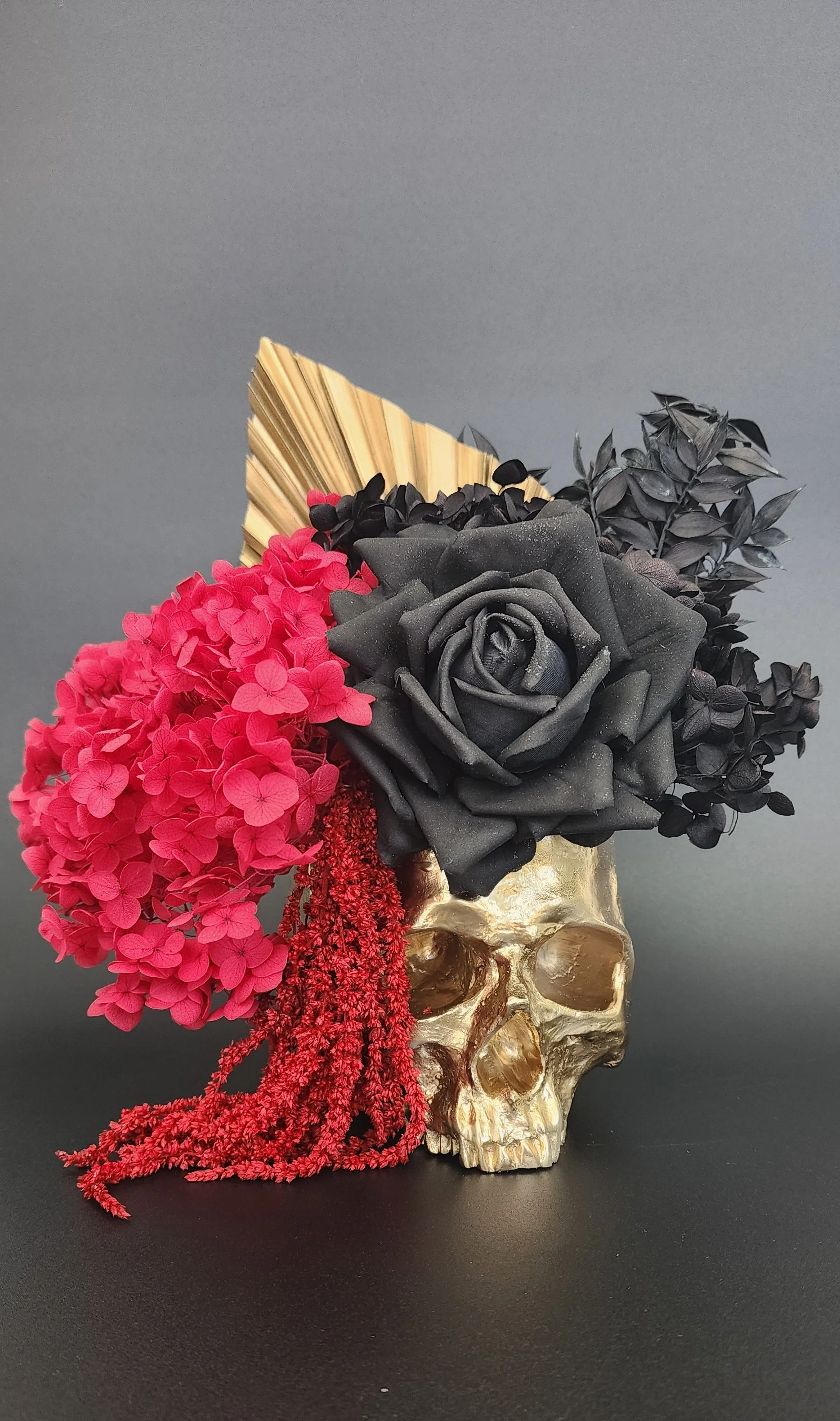 Decorative skull with black and red flowers and gold leaf, arranged on a black surface against a gray background.