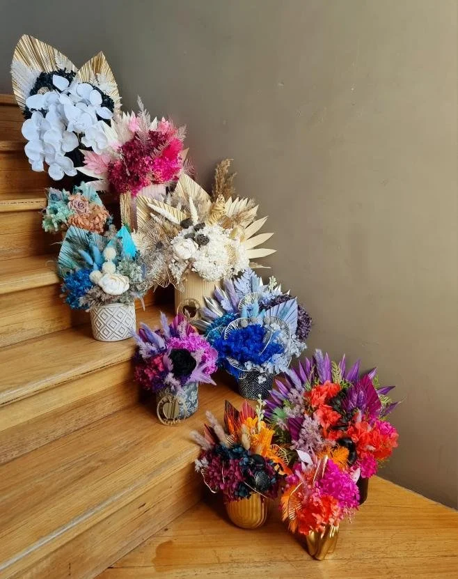 Multiple colorful flower bouquets arranged on wooden staircase steps with various colors, including white, pink, blue, purple, orange, and red, in decorative vases.