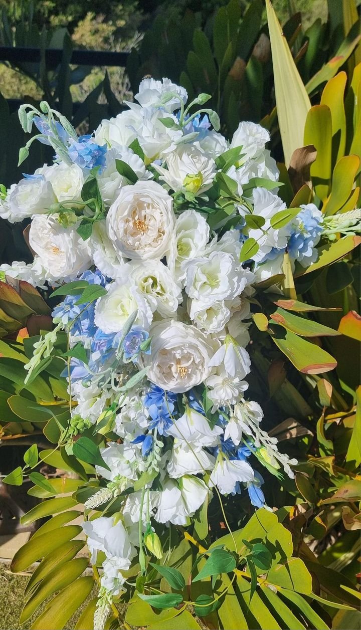 A floral arrangement with white and light blue flowers and green leaves, set outdoors among garden foliage.