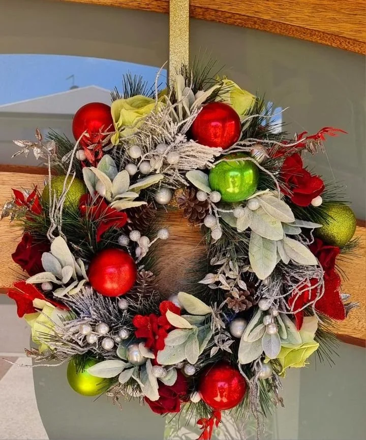 Festive Christmas wreath decorated with red and green ornaments, silver berries, pinecones, and frosted leaves hanging on a door.