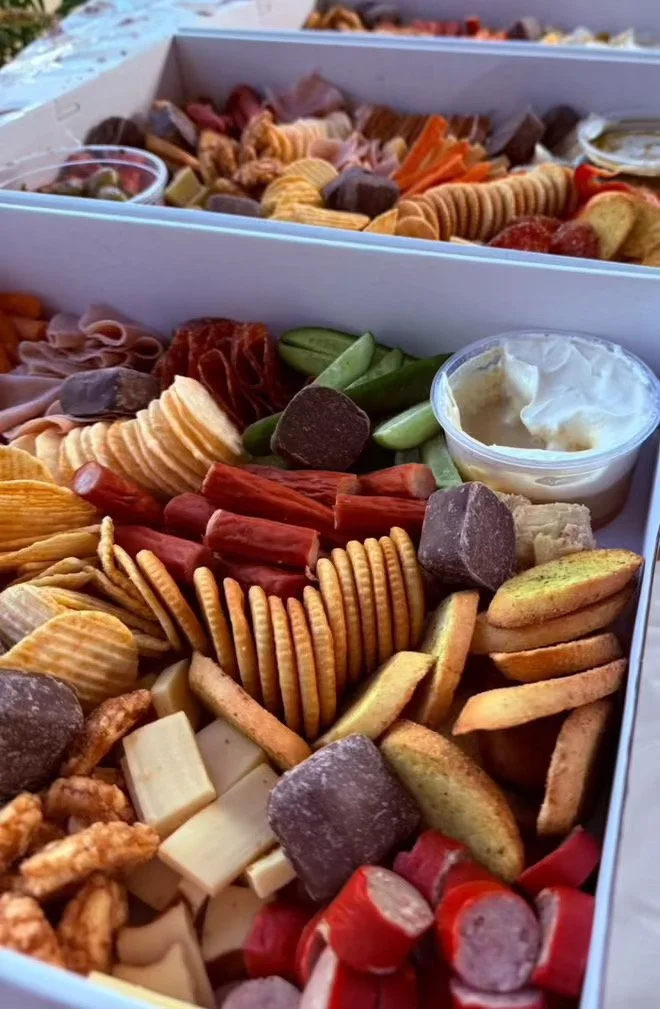 A close-up of a charcuterie board with assorted meats, cheeses, crackers, and chocolates, along with a small cup of mozzarella cheese.