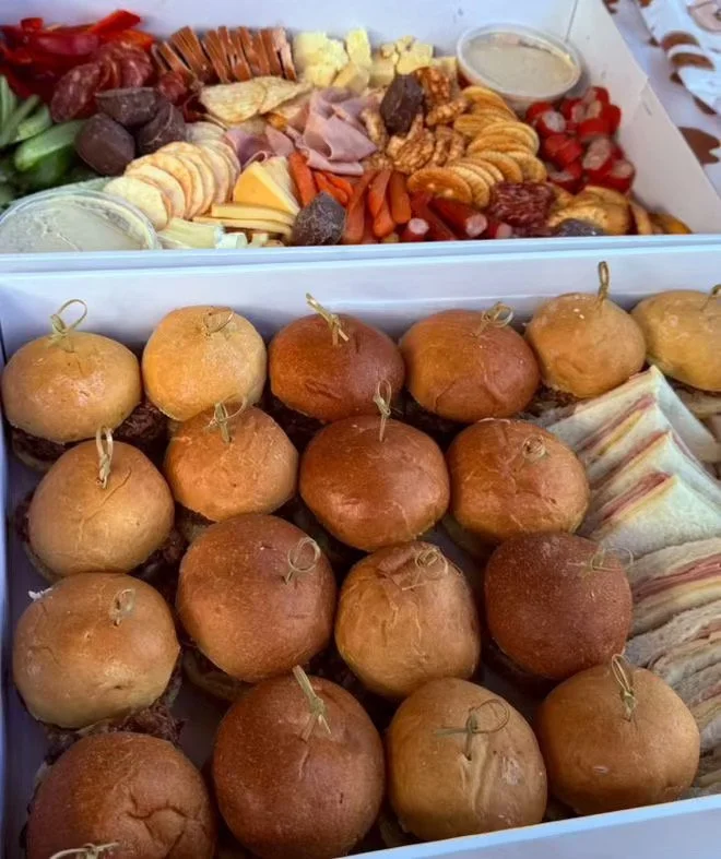 Tray of mini sliders with various fillings and a platter of assorted cheeses, crackers, meats, grapes, and dips.