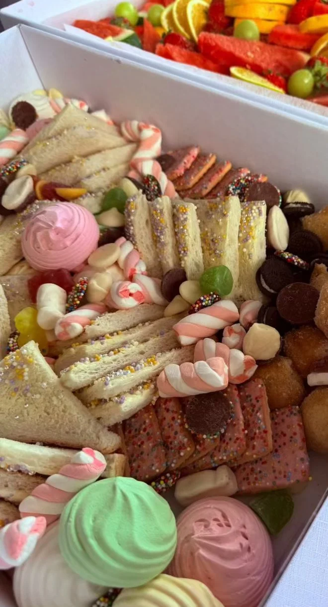 Assorted holiday treats and desserts, including mini sandwiches, colorful candies, cookies, and marshmallows in a decorative box.