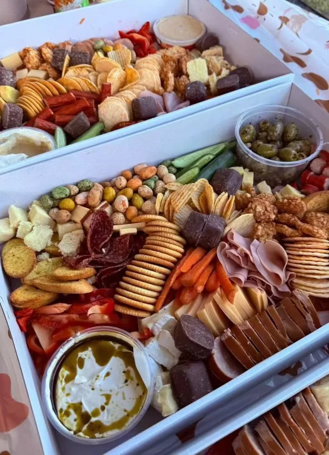 A large white tray with assorted snacks including crackers, cheese, meats, olives, vegetables, and dips.