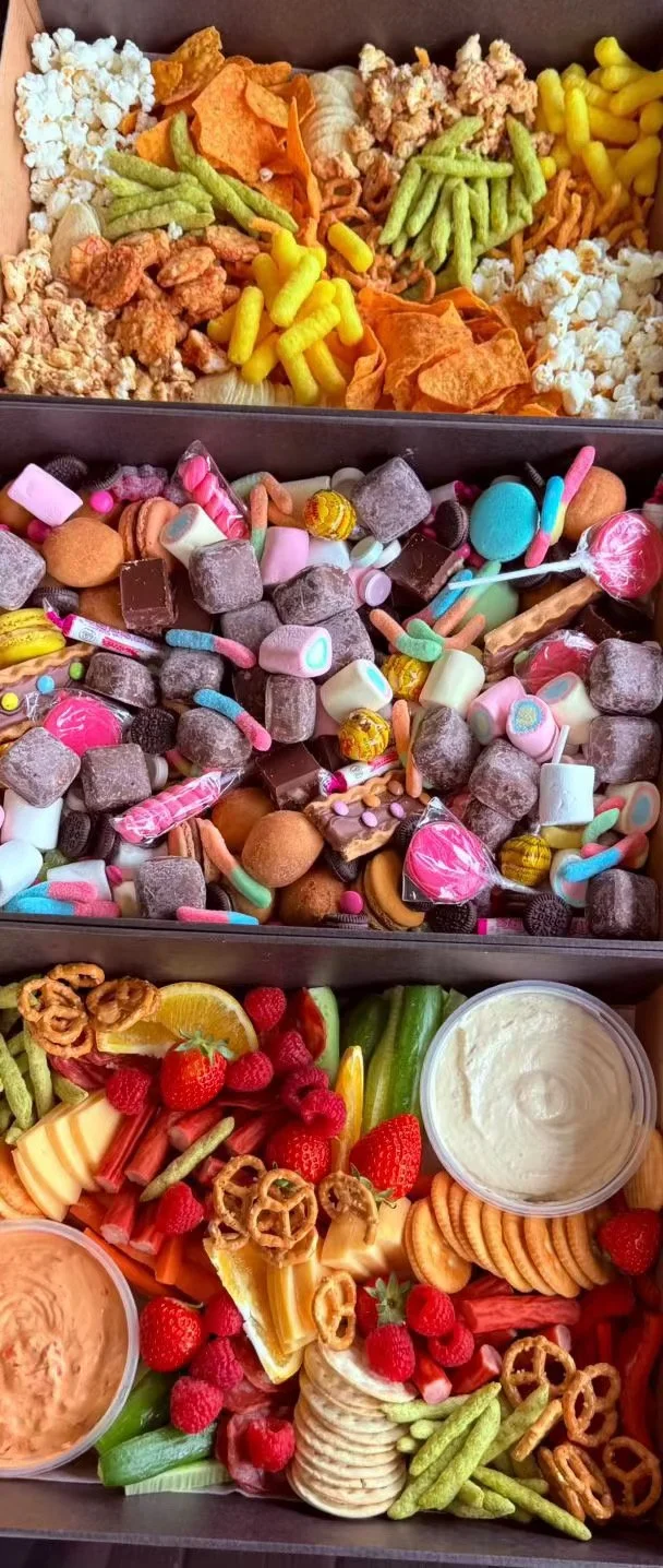 Three tiered tray with assorted snacks: top tier has popcorn, potato chips, cheese balls, and vegetable chips; middle tier contains various candies and sweets like marshmallows and chocolates; bottom tier features fresh strawberries, raspberries, veg