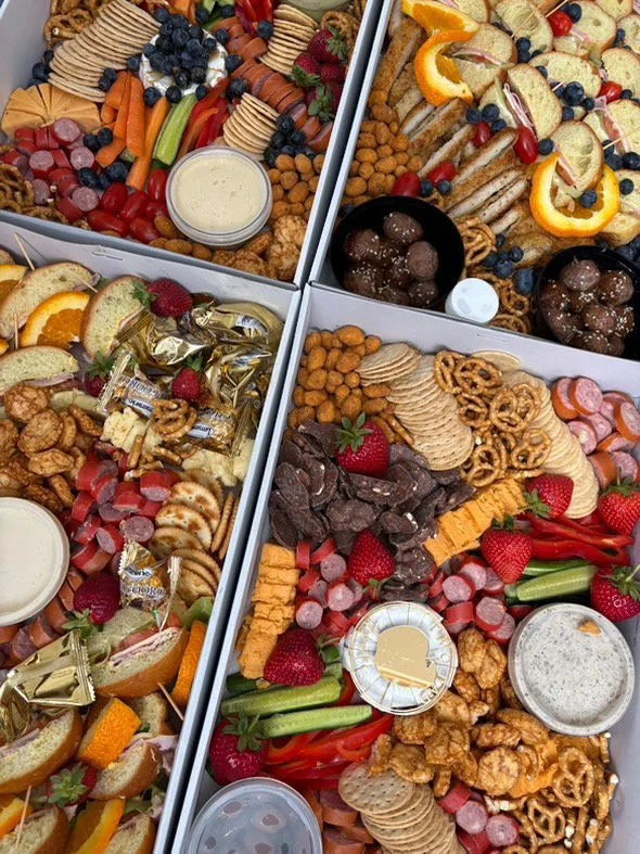 Three large food platters with an assortment of fruits, vegetables, cheese, crackers, chips, chocolate, and dipping sauces.