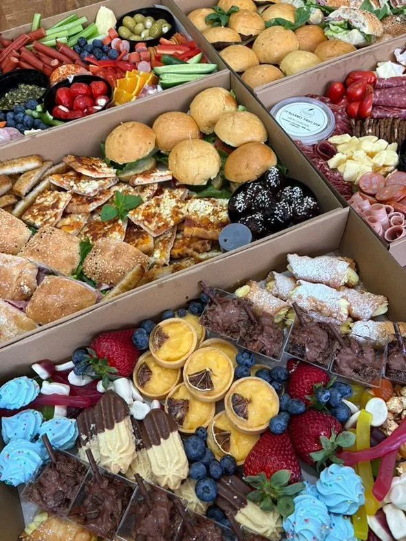 Assorted party snacks and desserts including mini sandwiches, fresh fruits, cupcakes, cookies, and candies arranged in three boxes.