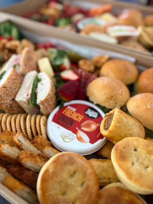 Assorted finger foods and snacks including mini sandwiches, crackers, cookies, chicken wings, and a container of onion dip.